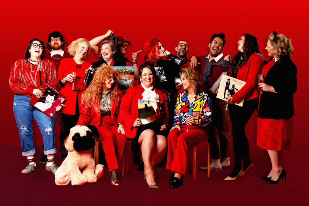 A group photo of the JayRay team decked out in rad '80s outfits against a red backdrop