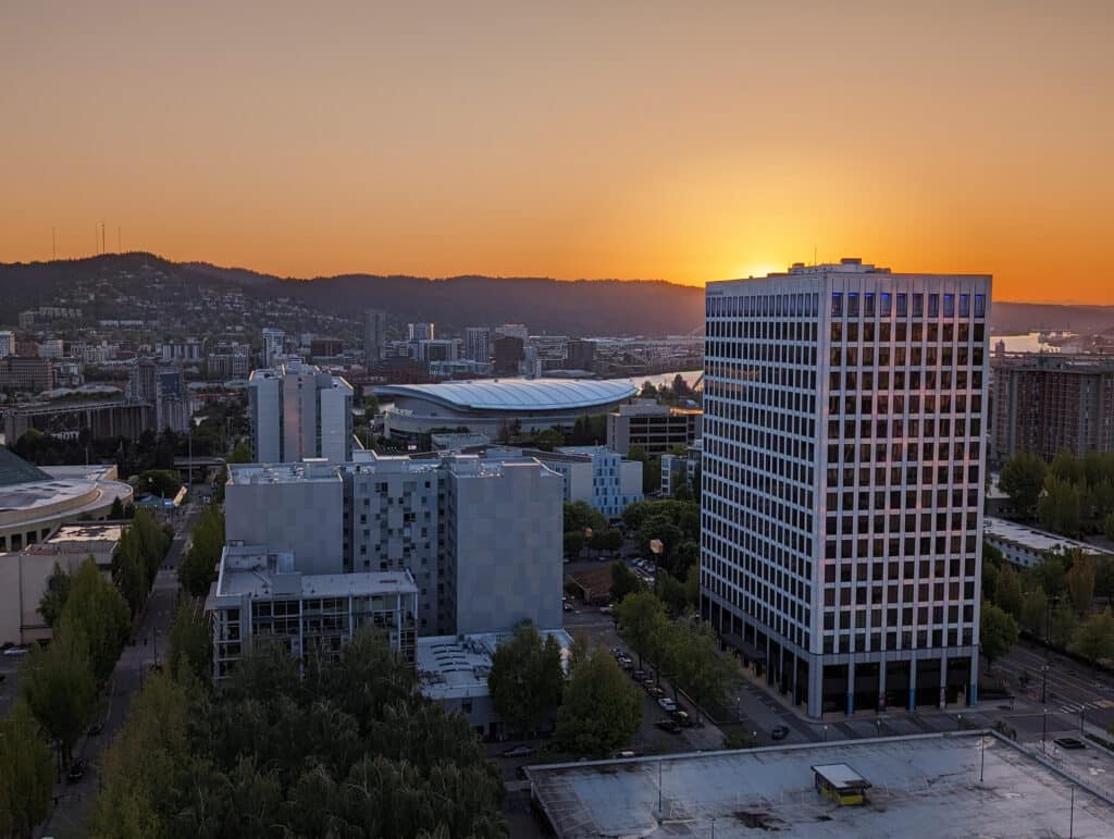 High-rise buildings and the Moda Center with the sun setting behind the West Hills in Portland.
