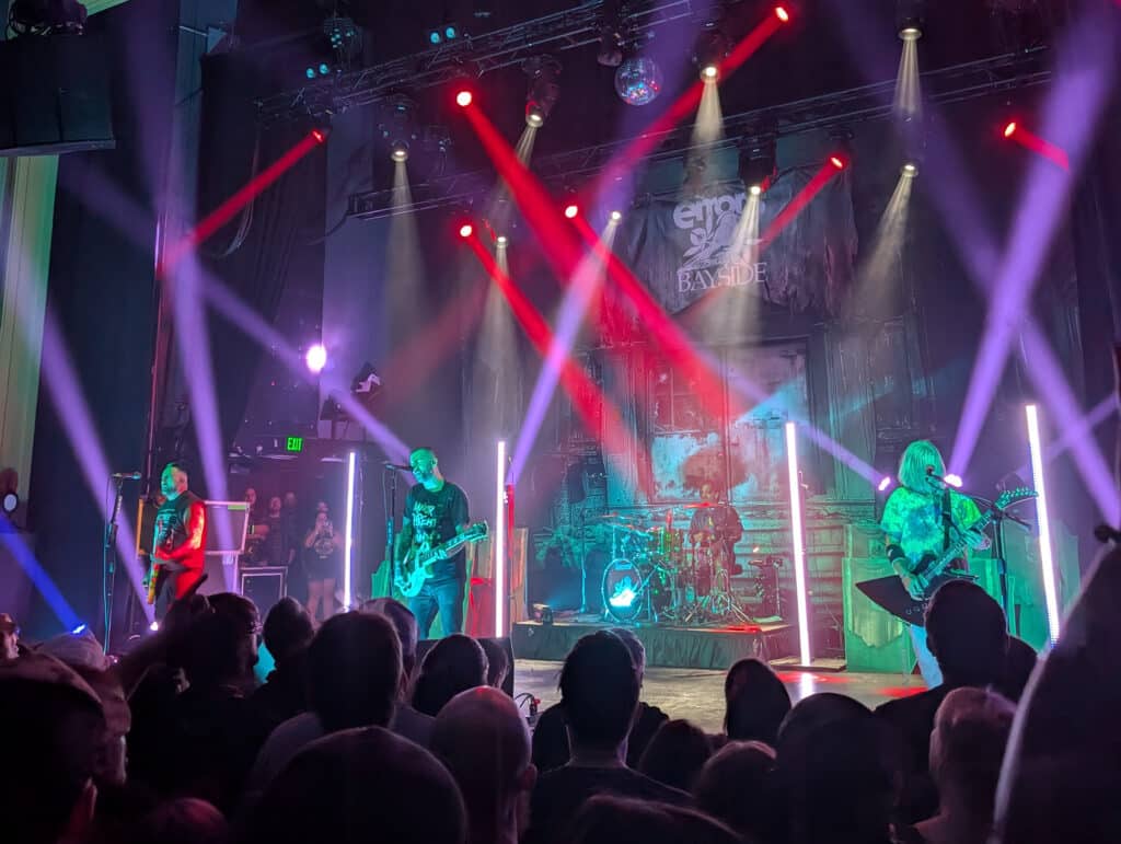 A rock band performing under colorful stage lights in front of a lively crowd.
