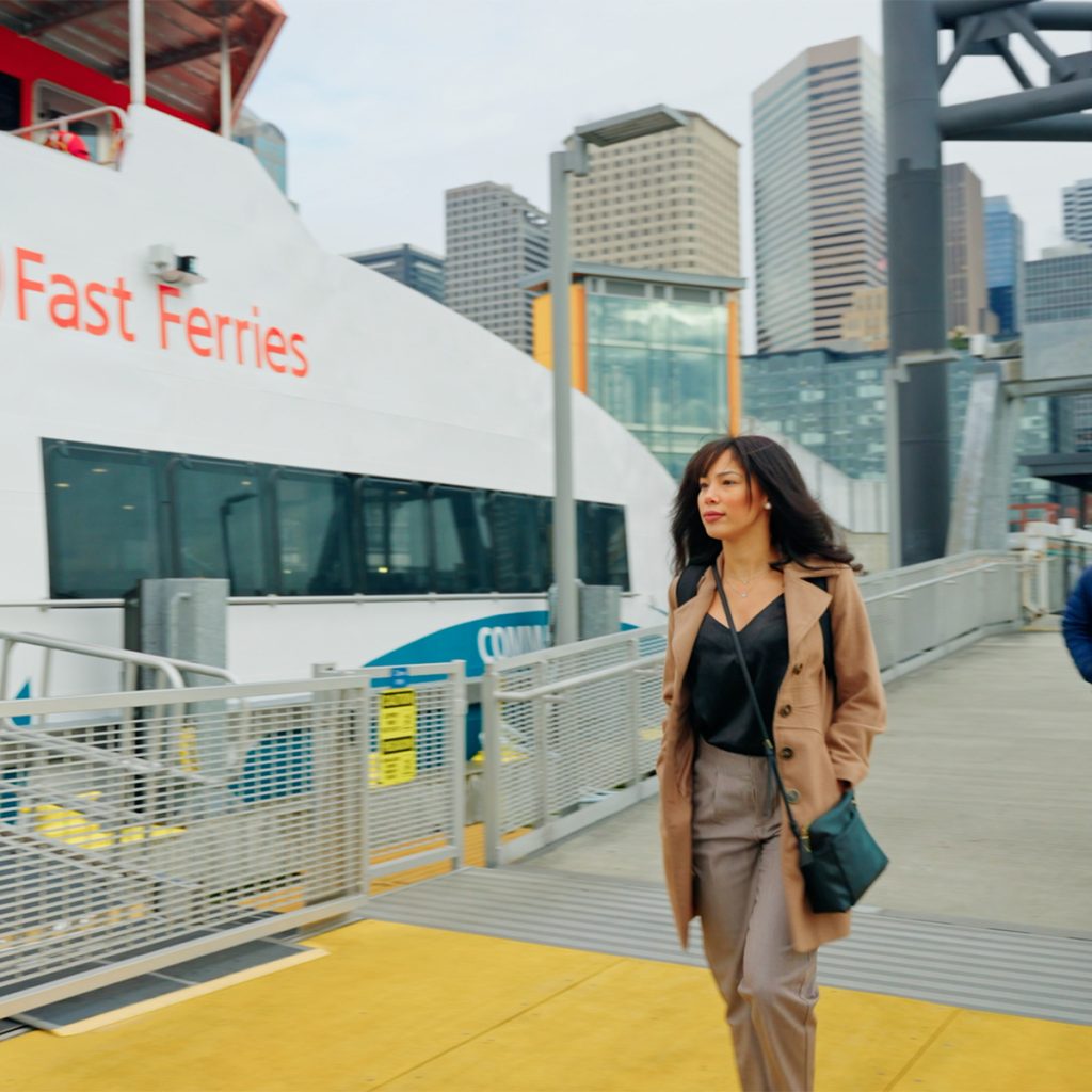 A woman in a coat walks along the dock to board a Fast Ferry.