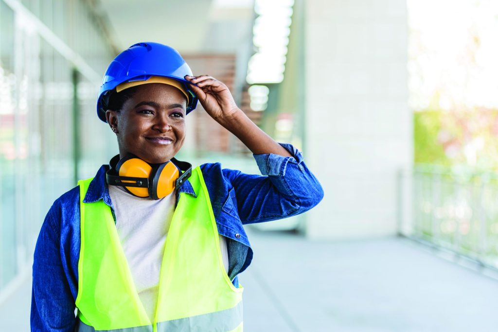 Photo of a person adjusting their hard hat and smiling while on a construction site