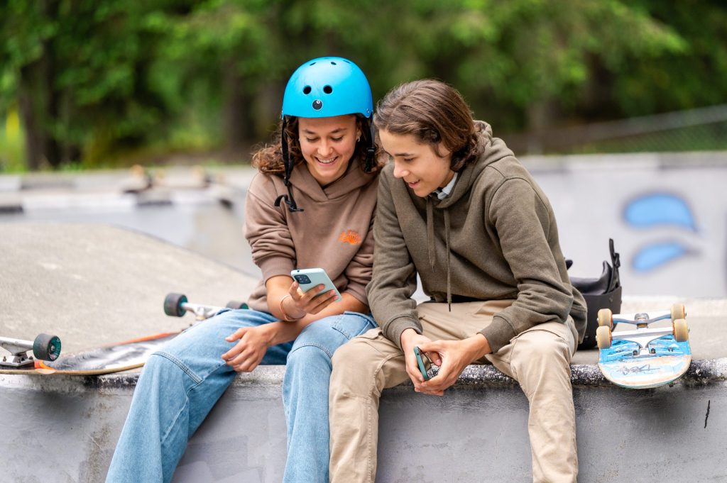 Photo of two teenagers looking at a phone while at a skatepark