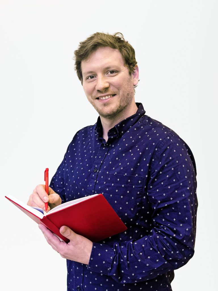 Alex Volkman holding a red notebook and pen