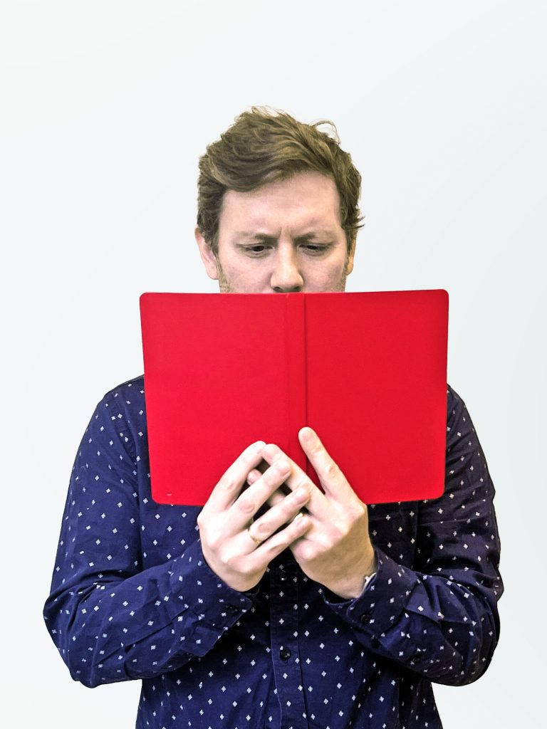 Alex Volkman frowns at a red notebook partially obscuring his face
