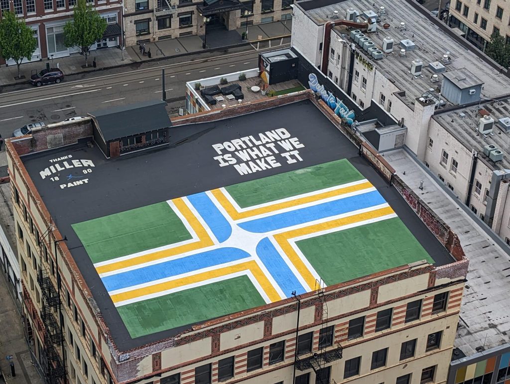 A rooftop shot in downtown Portland, Oregon, that has "Portland is what you make it" painted on the surface next to the Portland flag.