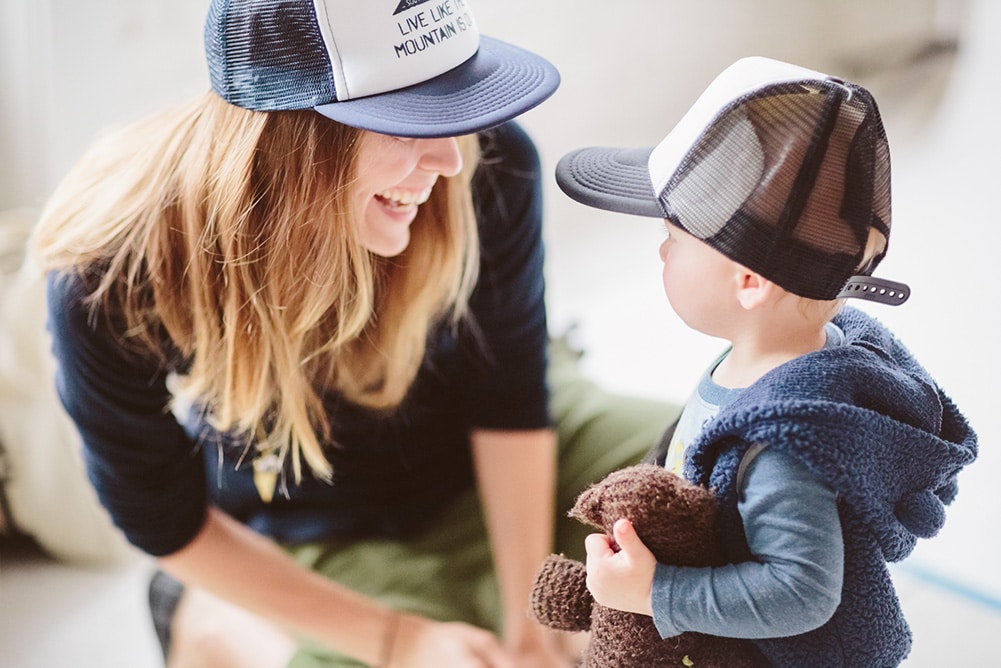 A woman and child smile at each other while wearing matching branded trucker hats