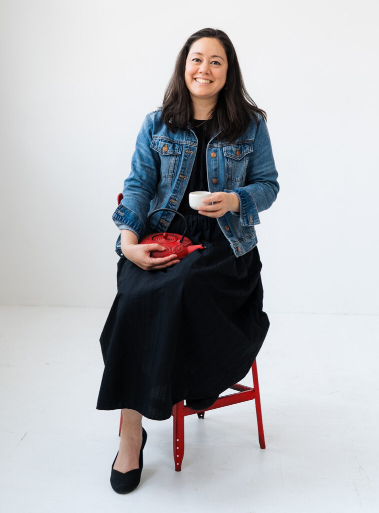 JayRay Communications Advisor Emilie Firn sitting in a vibrant red chair while holding a red tea kettle.