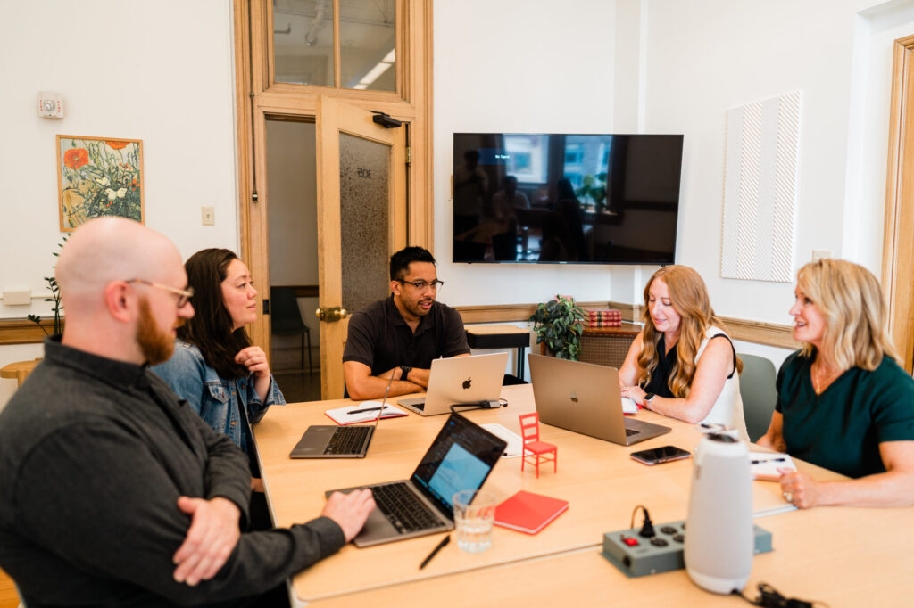 Several JayRay team members sit around a table with laptops in front of them