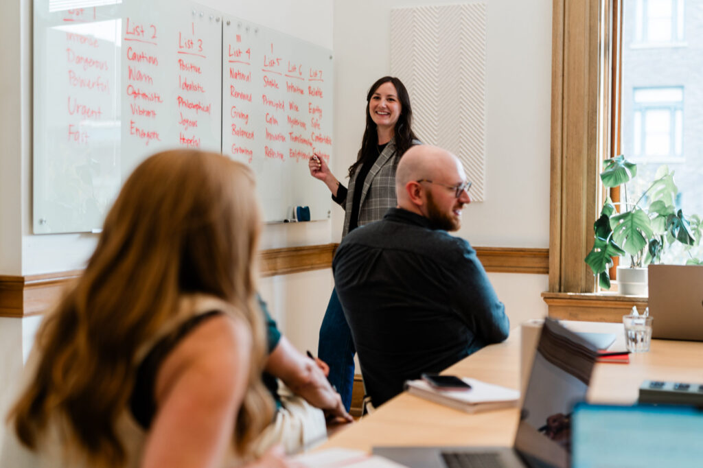 A woman leads a workshop by writing words in red marker on a whiteboard