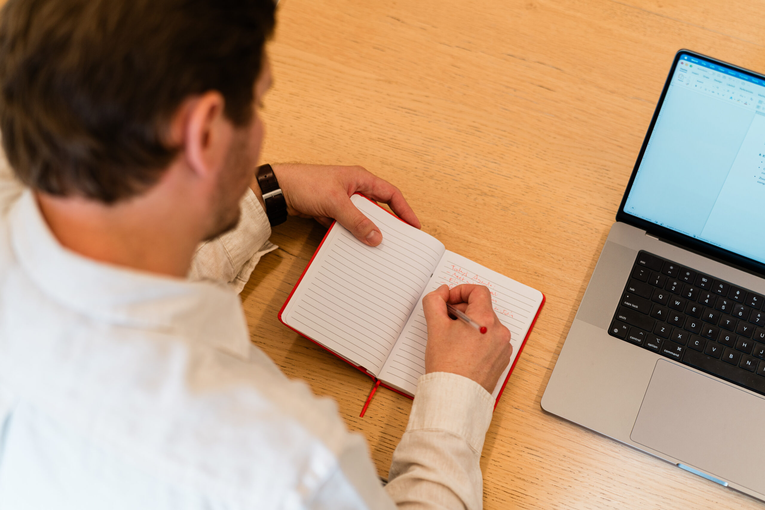 Over the shoulder view of a man writing in a red notebook