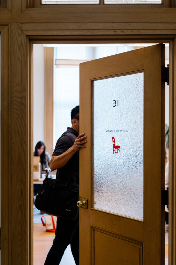 A man walks inside an office door labeled "JayRay" with the Red Chair logo